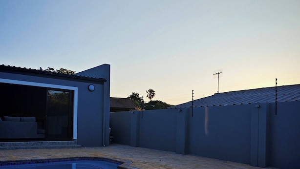 A swimming pool with a clear view of the surrounding area, including a building with a garage door and a fenced yard. - Room-king Deluxe Apartment-style Room (Cape Town)