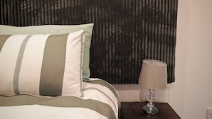 A bed with striped bedding, a dark curtain, and a lamp on a bedside table. - Room-king Deluxe Apartment-style Room (Cape Town)
