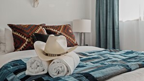 Una cama bien hecha con un edredón estampado, una toalla blanca enrollada y un sombrero de vaquero.