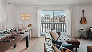 Una sala de estar moderna con mesa de fútbol, un sofá, una guitarra y un balcón con vista a la ciudad.
