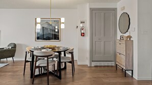 Un comedor con una mesa, sillas, una lámpara colgante, una obra de arte enmarcada y una puerta.