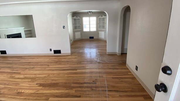 A spacious room with wooden flooring, white walls, and a large arched doorway leading to another room. - Charming basement separate entrance  2-bedroom house with AC in welcoming Pueblo (Pueblo)