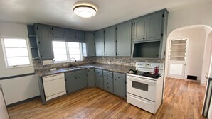 A kitchen with light blue cabinets, a white stove, and a window. - Charming basement separate entrance  2-bedroom house with AC in welcoming Pueblo (Pueblo)