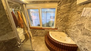 A bathroom with a glass shower enclosure, a bathtub, and a window with a view of buildings. - Nar Villa by the Sea (Alanya)