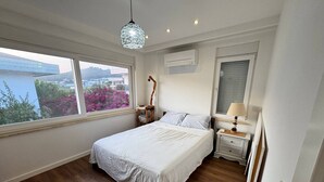 A bedroom with a bed, bedside table, lamp, air conditioning unit, and a view of the outdoors. - Nar Villa by the Sea (Alanya)