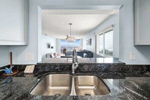 Una cocina moderna con un lavamanos doble, encimeras de granito y vista al área de estar.