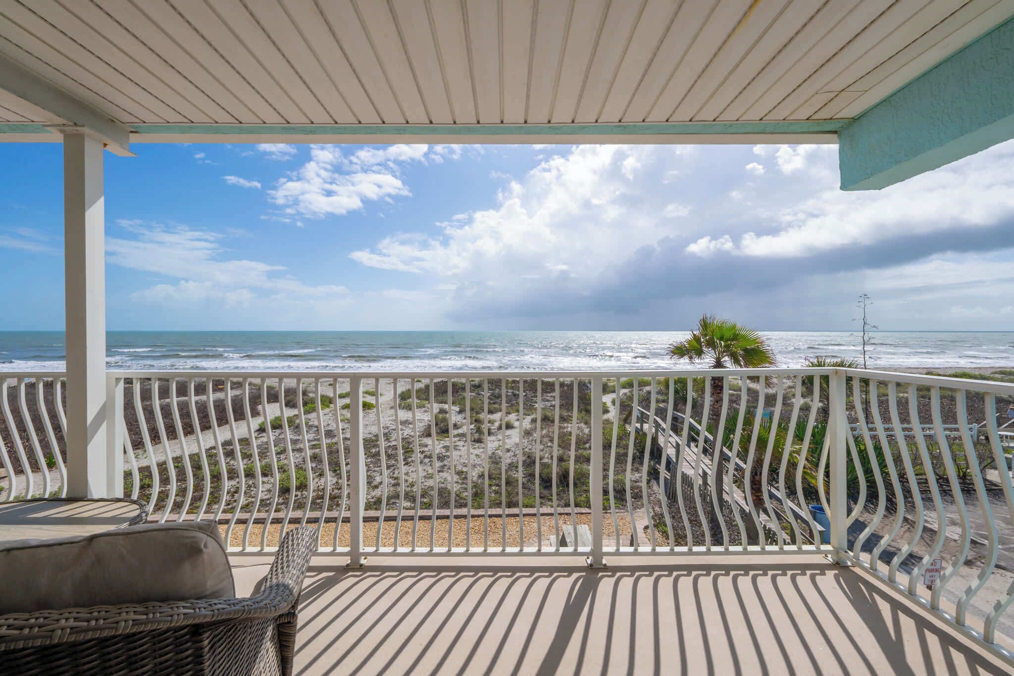 A covered balcony with a view of the beach and ocean.