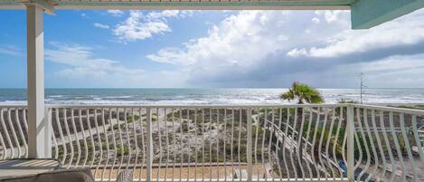 A covered balcony with a view of the beach and ocean.