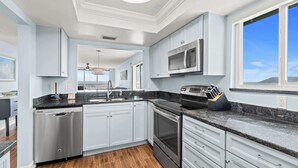 A modern kitchen with stainless steel appliances, white cabinetry, and a large window providing a view. - Oceanview I 3rd FL I Quiet Beach Escape I Beach (Cocoa Beach)