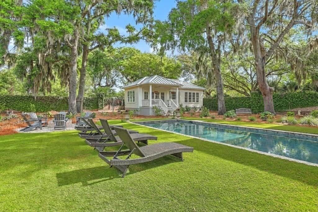 A pool with lounge chairs, a house with a porch, and trees with hanging moss.