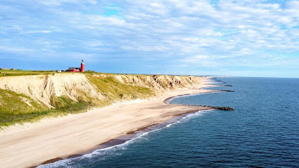 Ett kustlandskap med en fyr, en sandstrand och klippor.