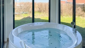 Ett bubbelbad med utsikt över en gräsklädd äng och en byggnad i bakgrunden.