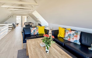 Un espacio tipo loft con un conjunto de sofás, una mesa de centro con un jarrón de flores y una mesa de fútbol.