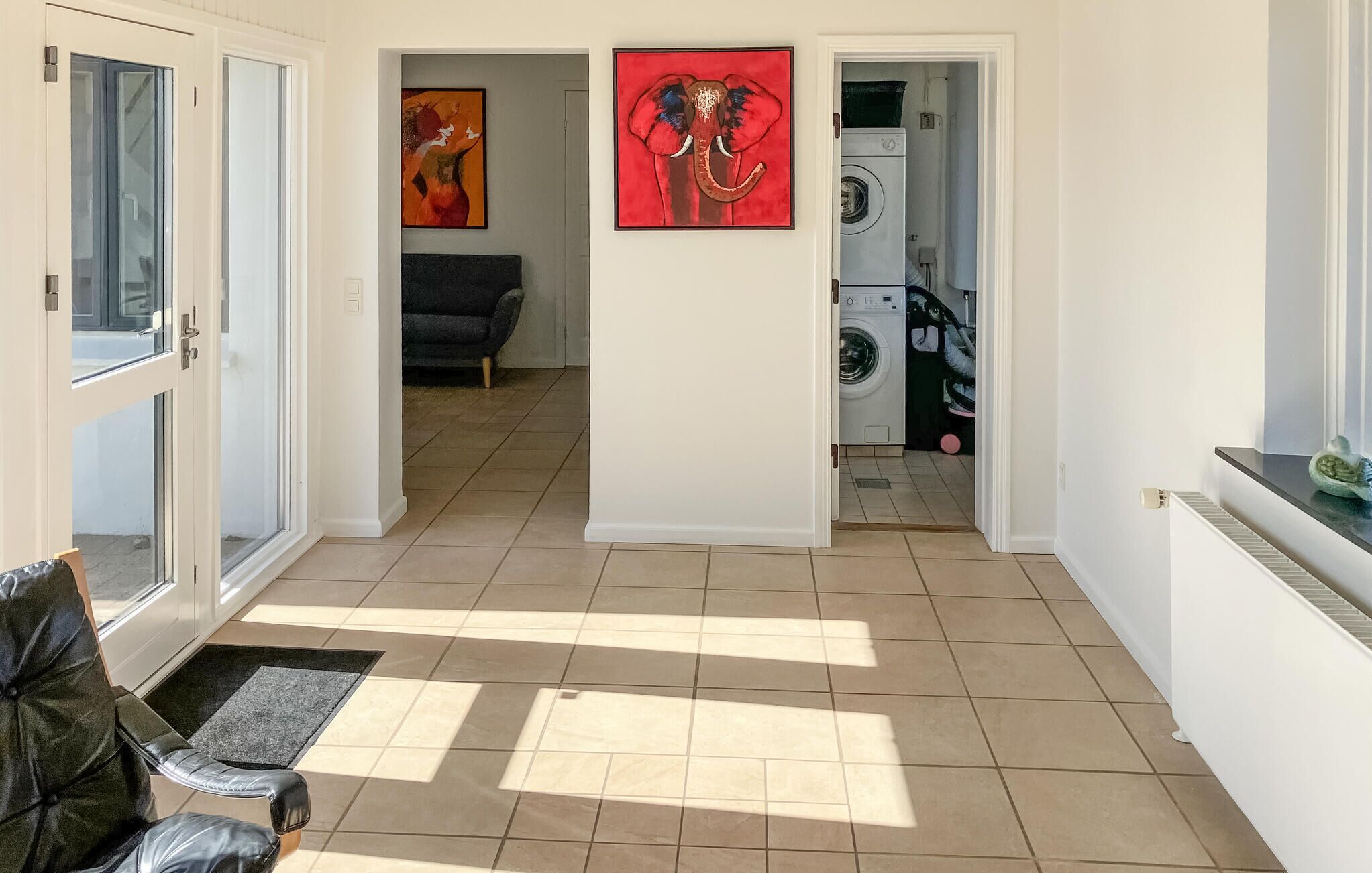 A hallway with a black leather chair, a red elephant painting, and a washing machine in the background.