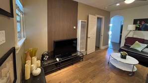 A living room with a flat-screen TV, wooden panel wall, and a black sofa.