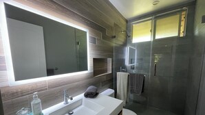 A modern bathroom with a large mirror, a white sink, a glass shower enclosure, and a toilet.
