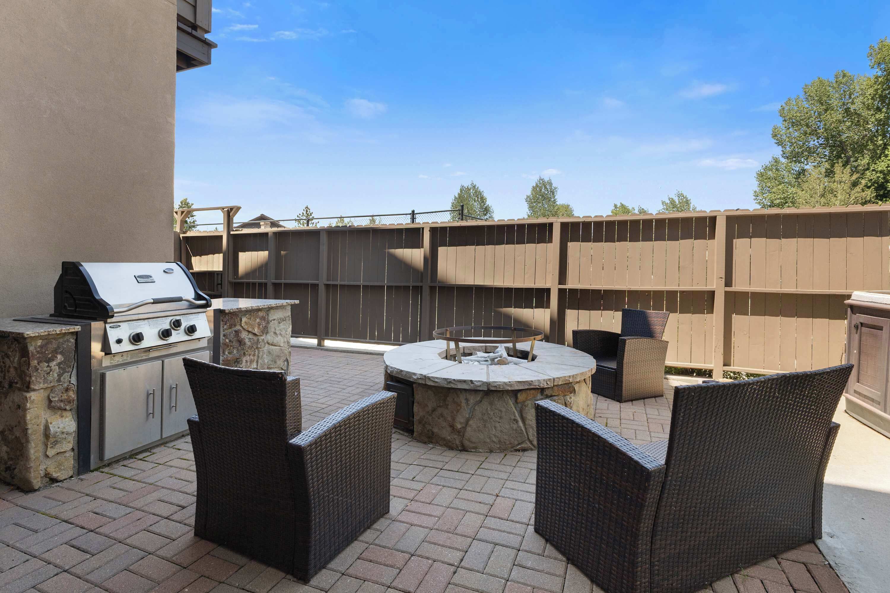 An outdoor patio with a grill, stone table, and wicker chairs.