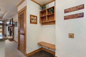 A hallway with a wooden door, a small shelf with plants, and two signs on the wall. - Aspen Oasis | 2BR, Private Hot Tub, Resort Pools (Steamboat Springs)