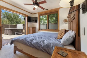 A bedroom with a bed, a ceiling fan, a TV mounted on the wall, and a window with a view of trees. - Aspen Oasis | 2BR, Private Hot Tub, Resort Pools (Steamboat Springs)