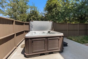 A hot tub with a wooden exterior, positioned outdoors with a wooden fence and trees in the background. - Aspen Oasis | 2BR, Private Hot Tub, Resort Pools (Steamboat Springs)