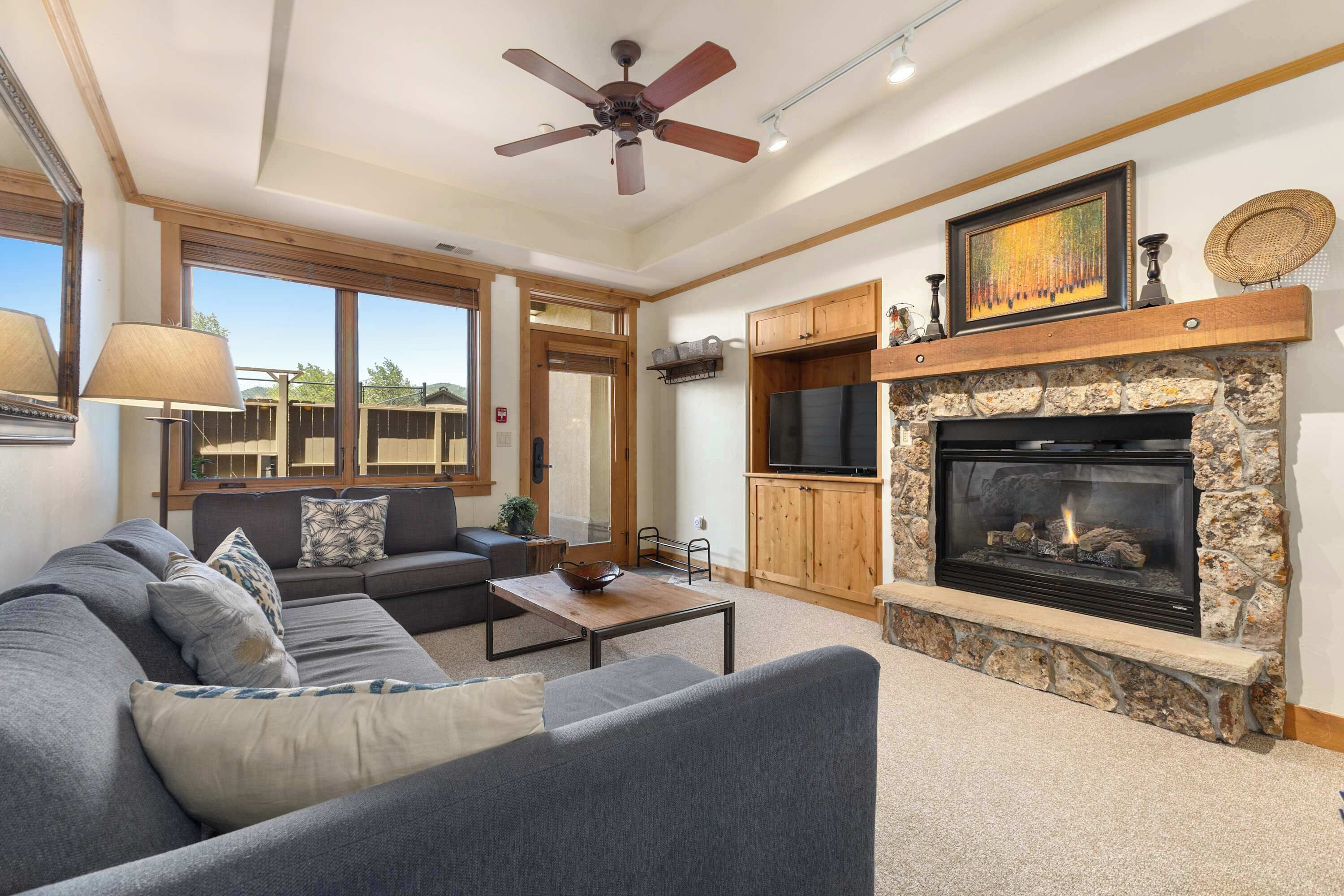 A living room with a fireplace, a ceiling fan, and a large window.