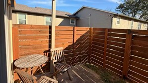 A covered patio with a wooden table and chairs, a wooden fence, and a view of neighboring houses. - Relax and Refresh at this Studio Apt. in South ATX (Austin)