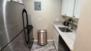 A compact kitchen with a stainless steel refrigerator, a trash bin, a sink, and white cabinets. - Relax and Refresh at this Studio Apt. in South ATX (Austin)