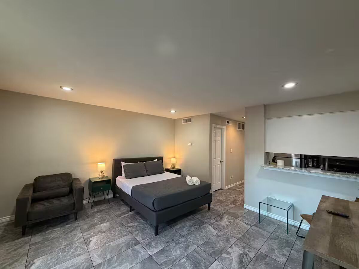 Une chambre comprenant un lit, une chaise, une table de chevet, un bureau et un coin cuisine.