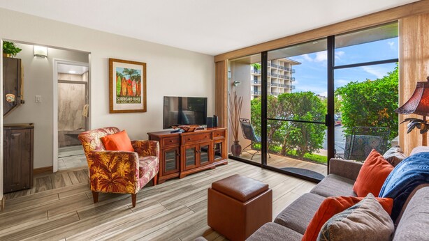 A modern living room with a flat-screen TV, a sofa, a coffee table, and a dining area with a wooden cabinet. - Double Master 2BR Villa | Pacific Shores | Kihei (Kihei)