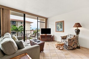 Una sala de estar con sofá, sillón, televisor y lámpara.