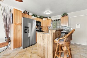 Une cuisine avec des meubles en bois, un réfrigérateur en acier inoxydable, un four à micro-ondes et un tabouret de bar.