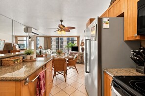 A kitchen with a central island, wooden cabinets, a refrigerator, and a stove. - Top Floor Ocean View | Central AC | Walk to Beach (Kihei)