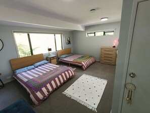 A bedroom with two beds, a dresser, a nightstand, a dreamcatcher, and a window. - Hosts on the Coast Pohutukawa Perch (Whitianga)