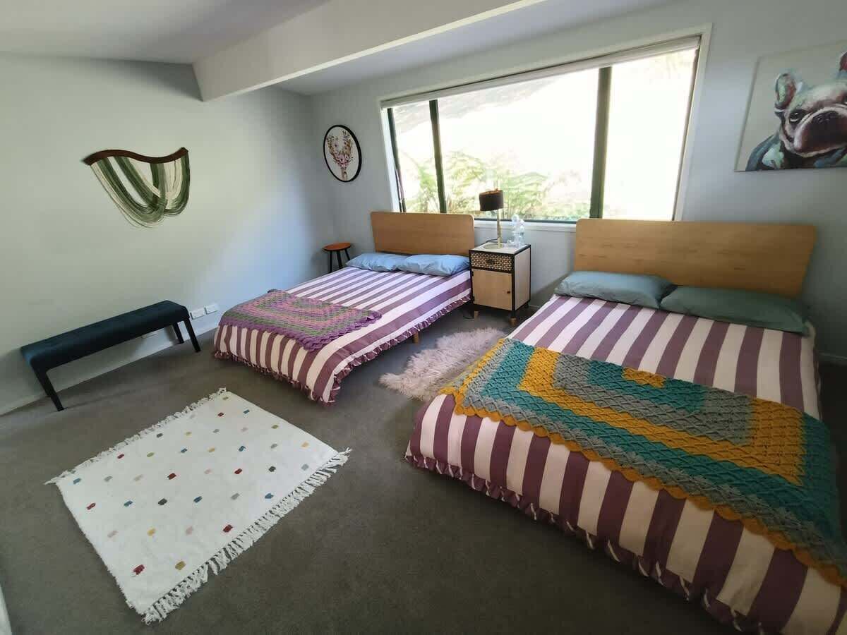 Un dormitorio con dos camas, un banco, una mesita y una ventana con vistas.
