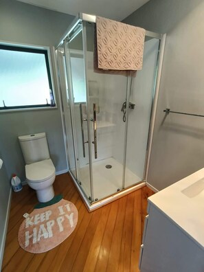 A bathroom with a glass-enclosed shower, a toilet, and a sink. - Hosts on the Coast Pohutukawa Perch (Whitianga)