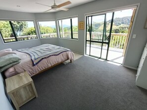 Een slaapkamer met een bed, een houten nachtkastje, een plafondventilator en een grote schuifdeur naar een balkon met uitzicht op groen.