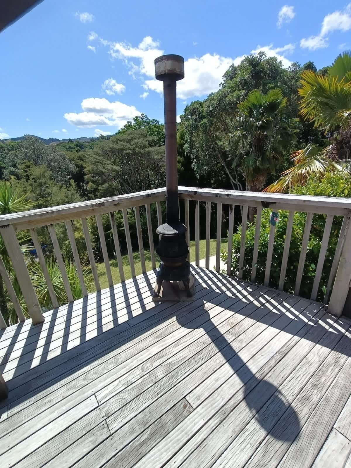 A wooden deck with a railing, a metal pole, and a view of a forested landscape.