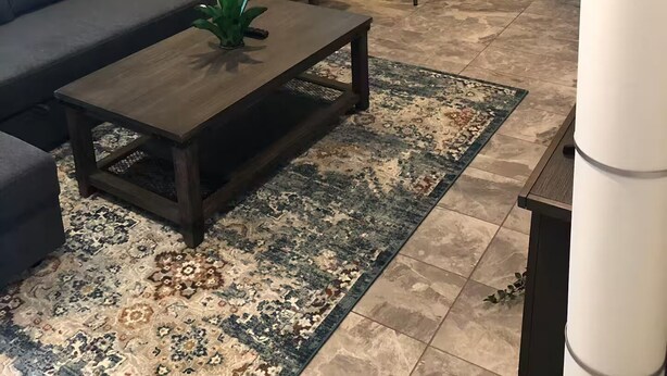 Ein Wohnzimmer mit einer Couch, einem Couchtisch, einem Teppich, einem Barhocker und einer Küchenzeile mit Arbeitsplatte und Schränken.