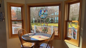 A dining area with a table and chairs, large windows with a view of a yard, and a stained glass window above the table. - Enjoy a bed & breakfast with view of Lake Huron, sunrises and eagles! (Ocqueoc)