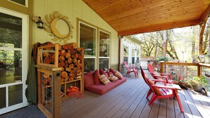 A covered porch with a wooden ceiling, a red sofa with cushions, and a wooden log display.