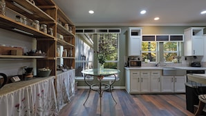 A kitchen with wooden shelves, a glass table, white cabinets, and a view of trees through the windows.