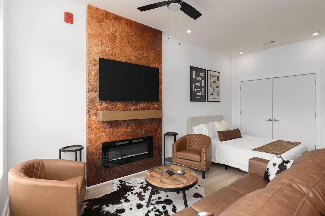 Una sala de estar moderna con chimenea, televisor montado en la pared, cama con cabecera y alfombra de cuero de vaca.