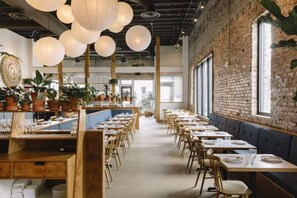 En restaurant med lange borde, træstole, hængende papirlanterner og plantekasser.