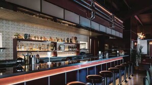 Een bar met een lange toonbank, krukken en diverse flessen.