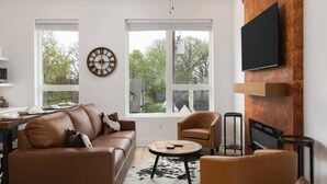 Een moderne woonkamer met een bank, fauteuil, rond salontafel en een flatscreen televisie bevestigd aan een houten wand.