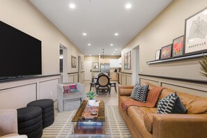Una sala de estar moderna con un televisor de pantalla plana, un sofá de cuero, una mesa de centro y un comedor al fondo.