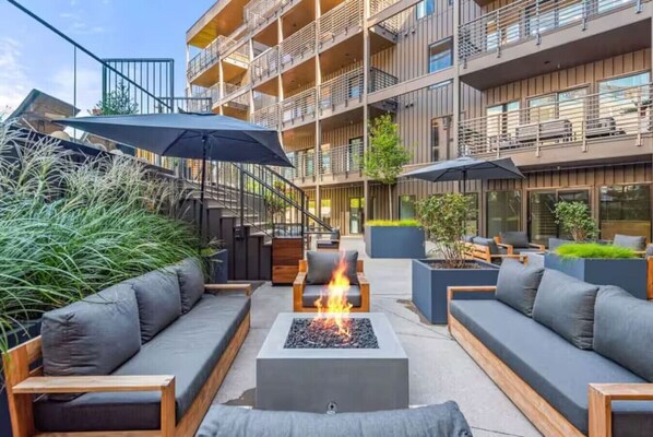 An outdoor seating area with sofas, a fire pit, and umbrellas.