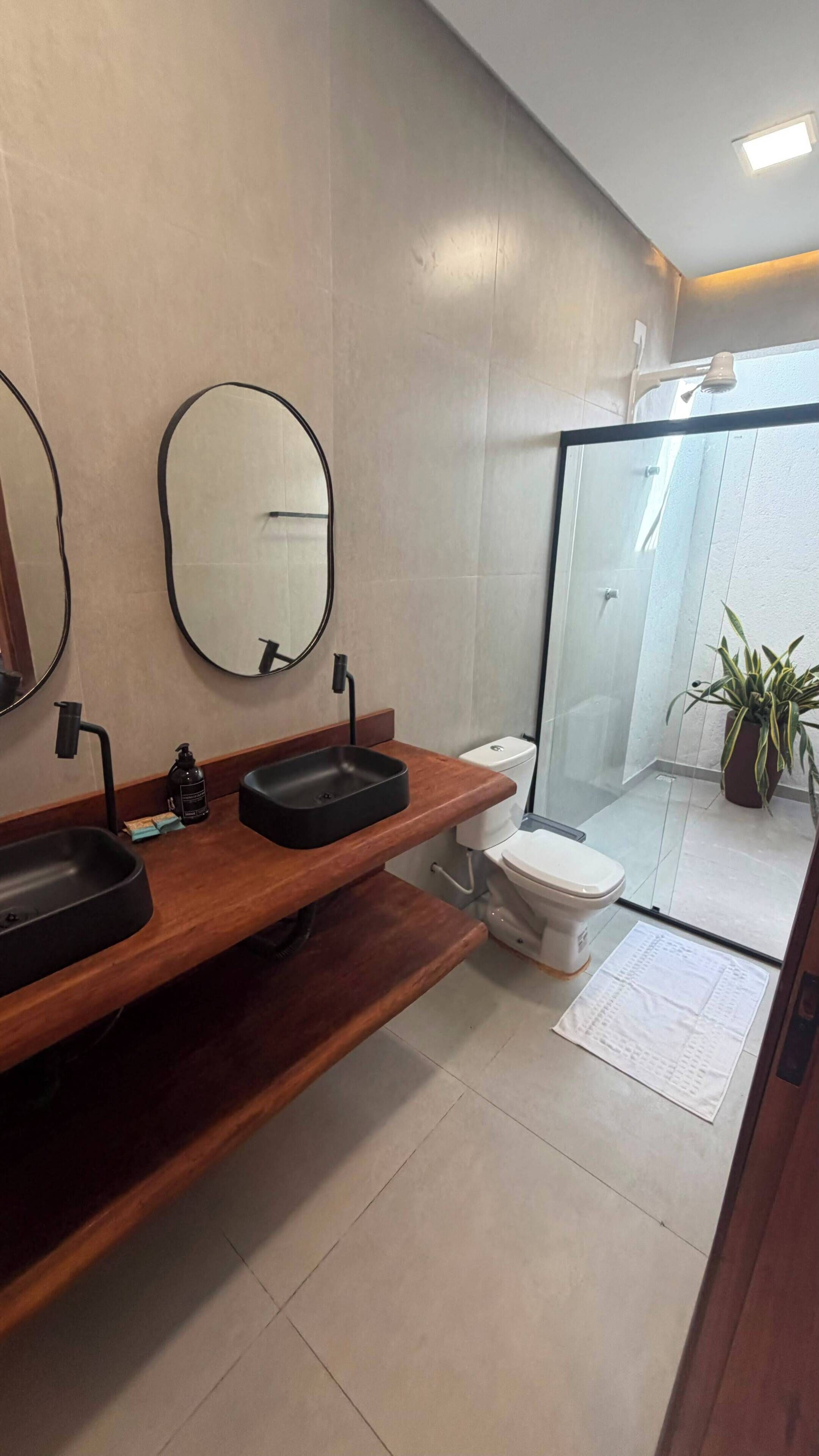 Een moderne badkamer met een houten wastafel, twee wastafels, een toilet en een douchecabine van glas.