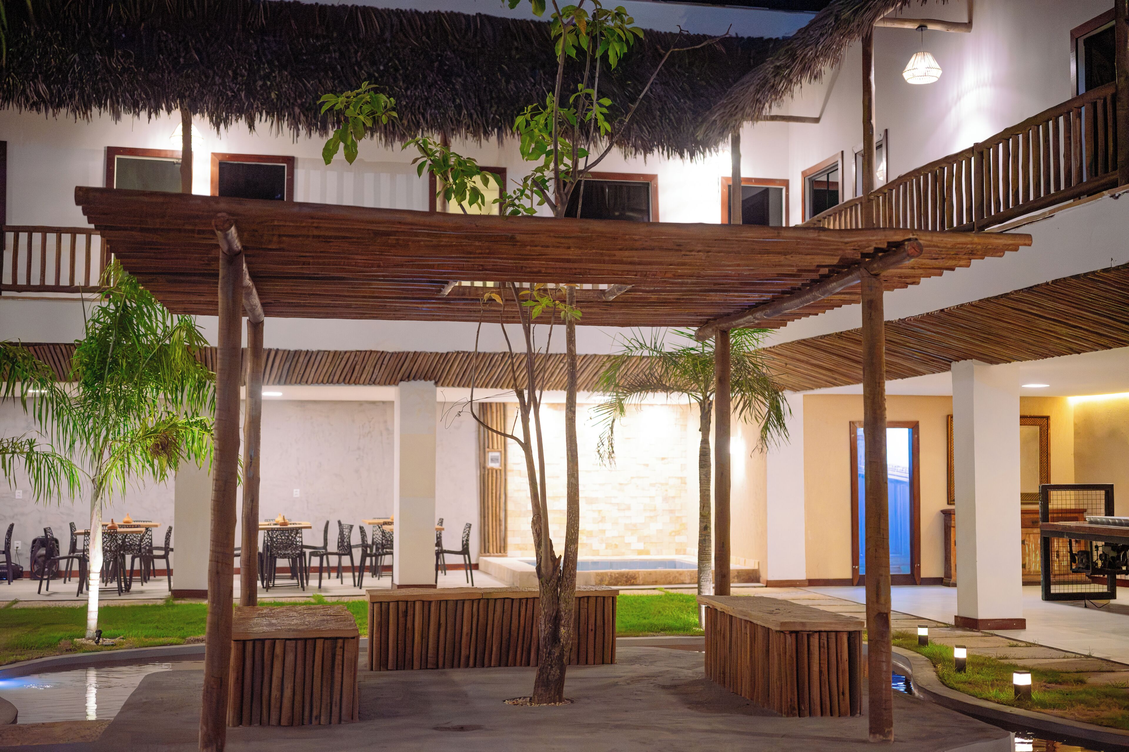 Un espacio al aire libre techado con bancos de madera, una piscina y un comedor con mesas y sillas.