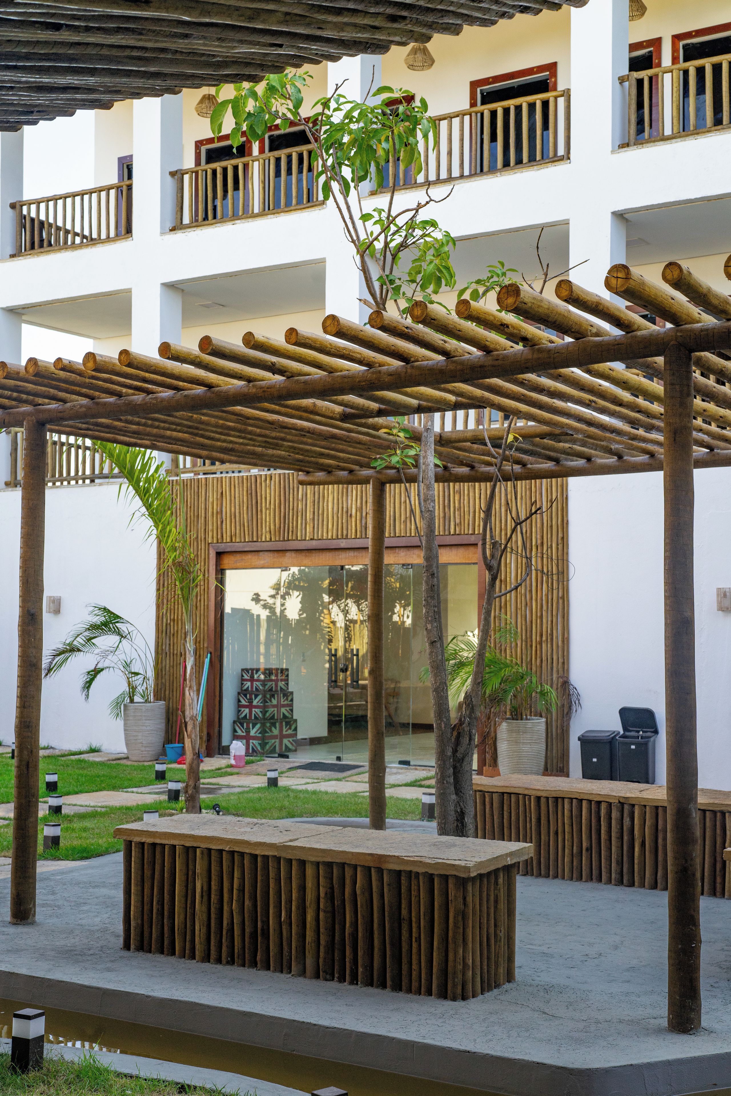 A courtyard with a wooden pergola, a seating area, and a building with balconies.